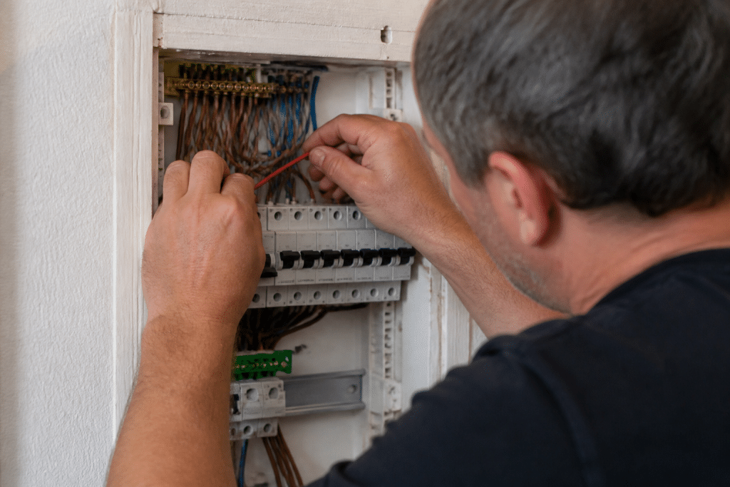 Electricien installant fil rouge dans tableau electrique mural