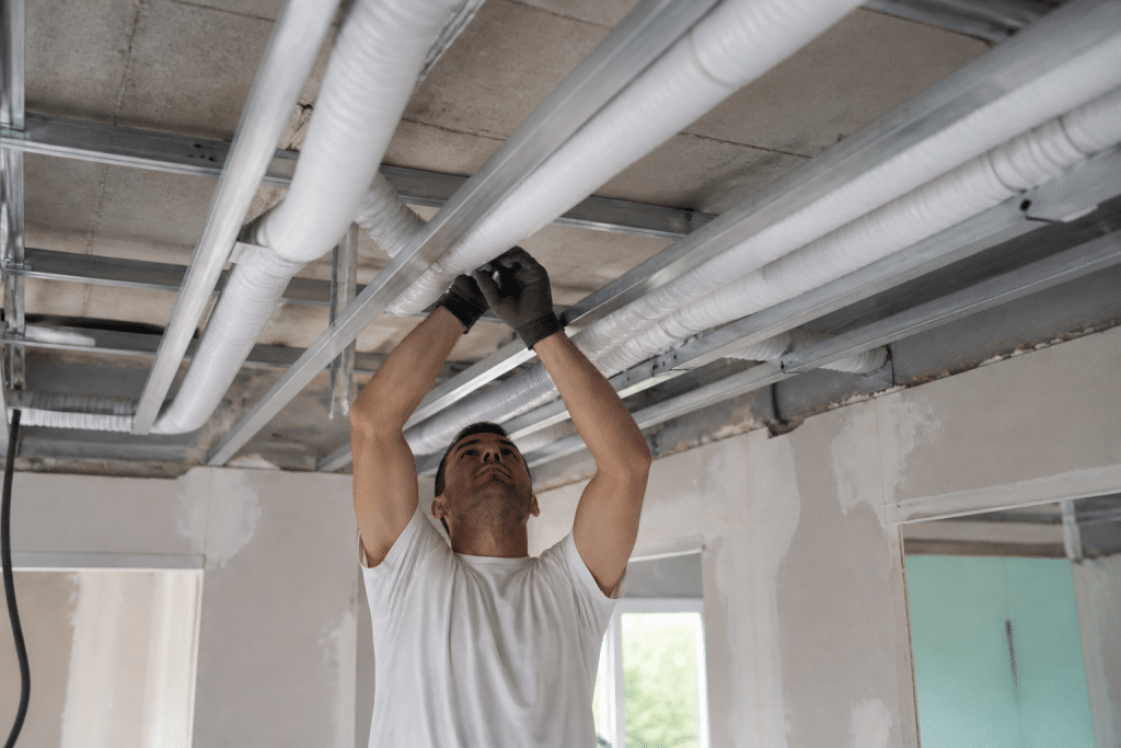Technicien installant conduits VMC blancs dans plafond