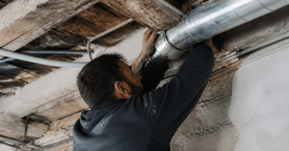 Technicien installant tuyauterie ventilation dans plafond ancien bâtiment