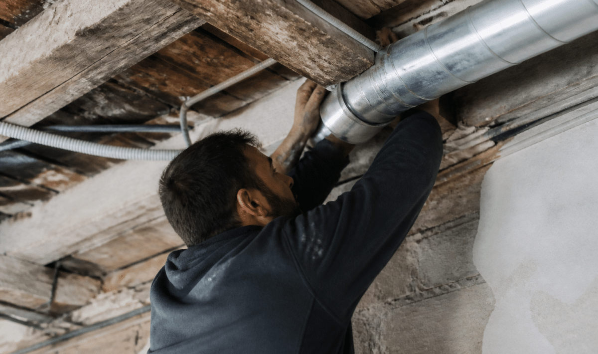 Technicien installant tuyauterie ventilation dans plafond ancien bâtiment
