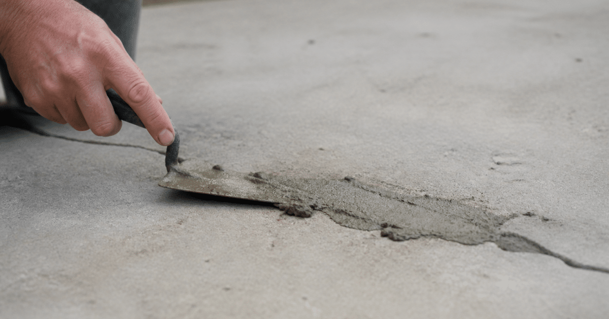 Truelle appliquant mortier gris sur fissure béton horizontal