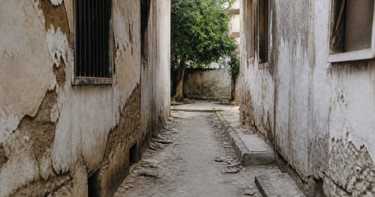Rue étroite entre immeubles dégradés, murs fissurés, détritus au sol