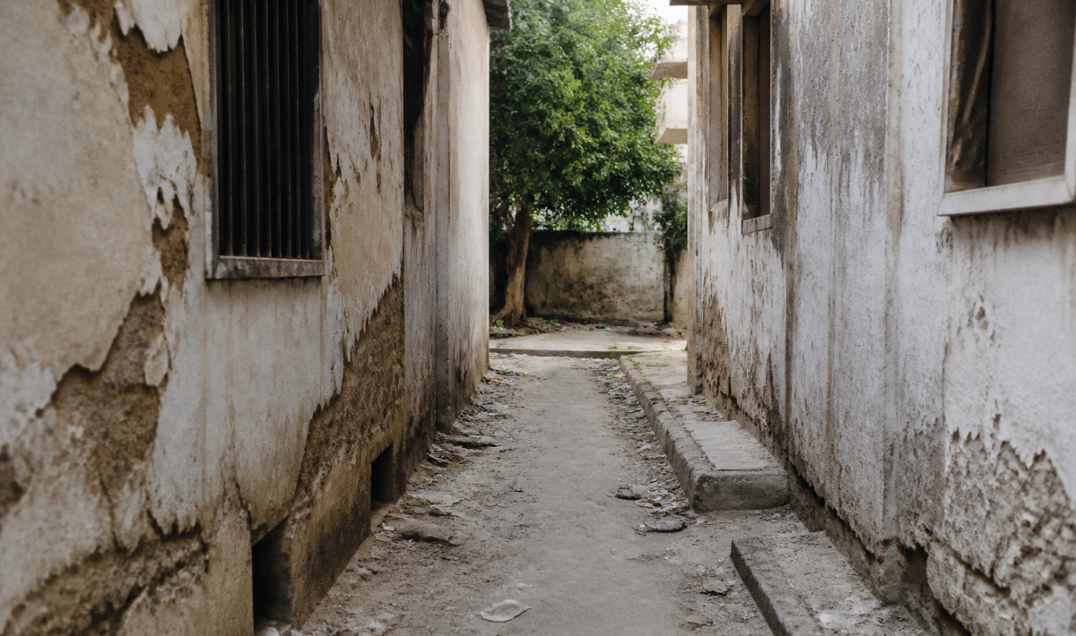 Rue étroite entre immeubles dégradés, murs fissurés, détritus au sol