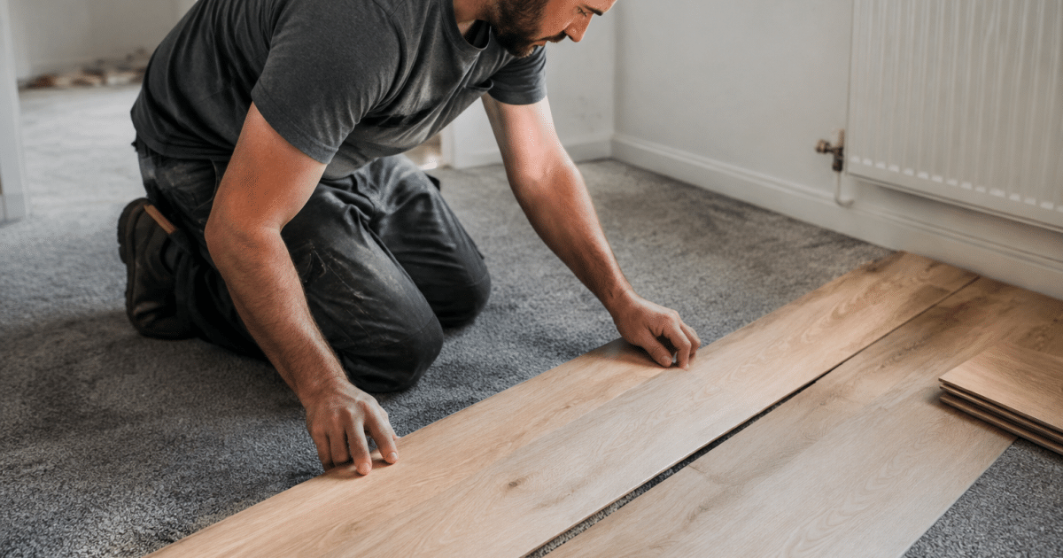 Ouvrier posant planches bois sur moquette grise existante