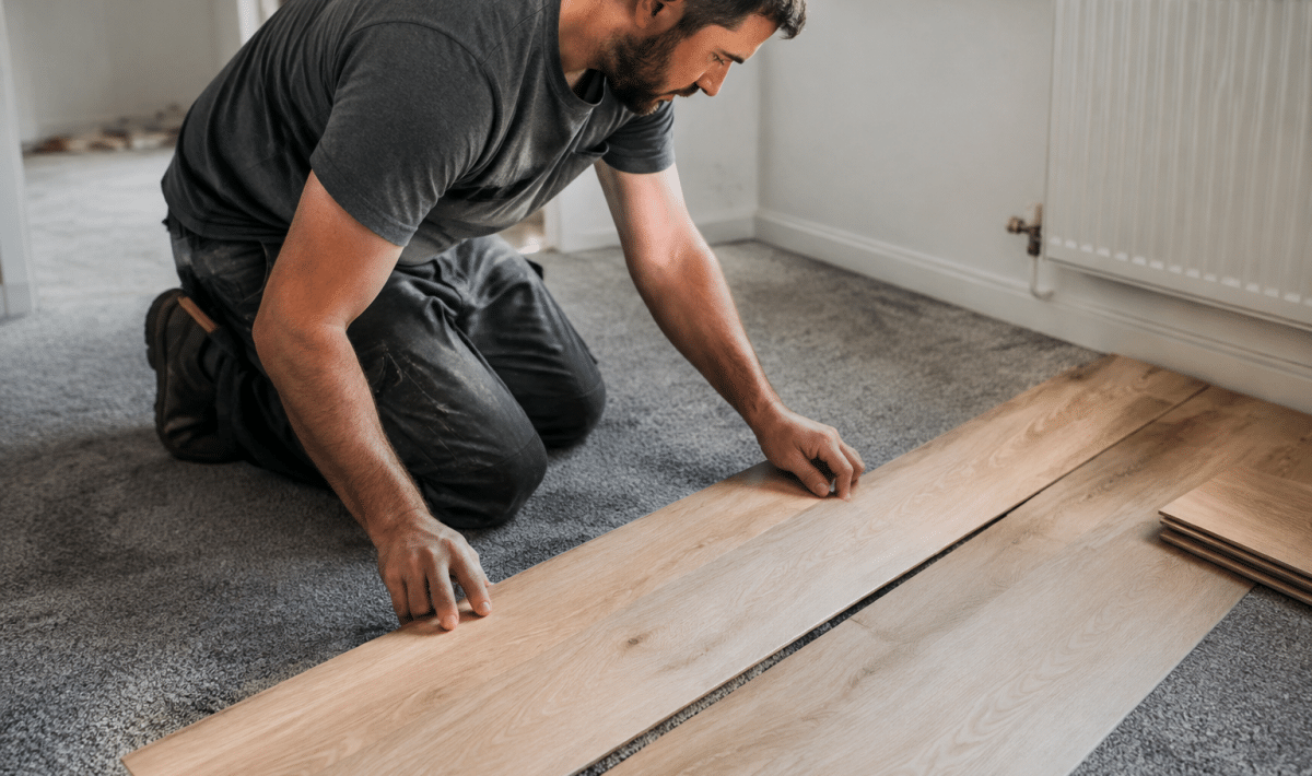 Ouvrier posant planches bois sur moquette grise existante