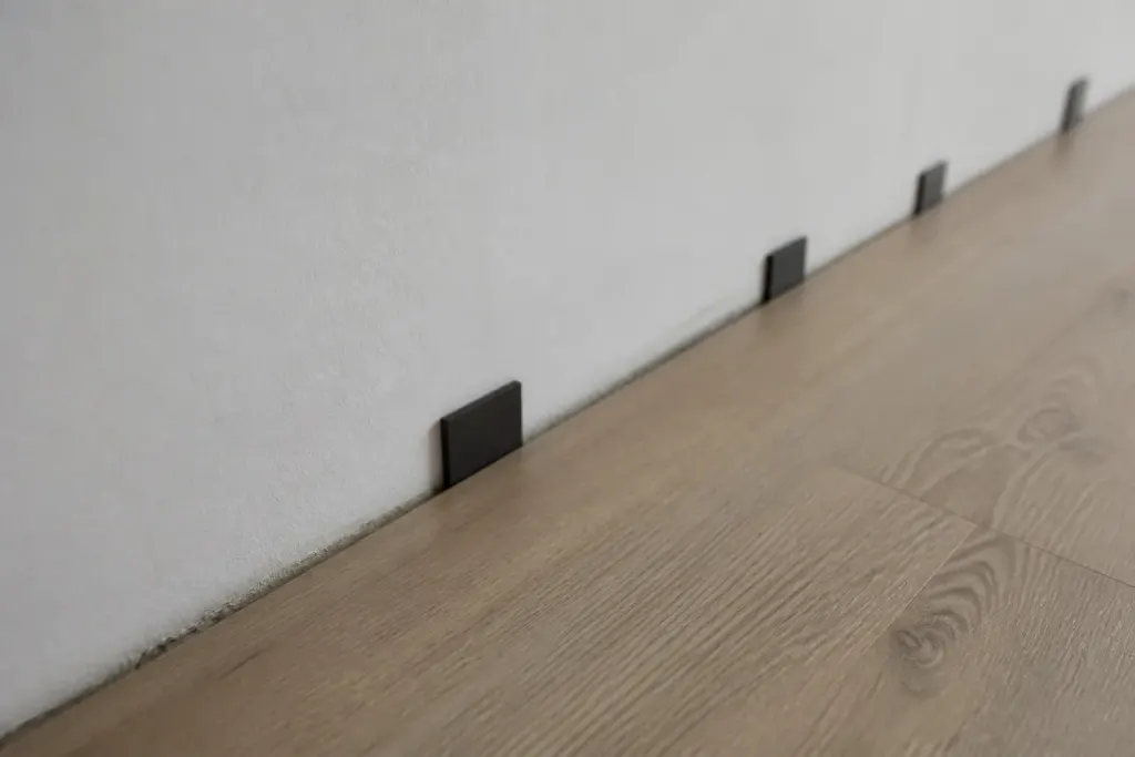Cales espaceurs visibles entre parquet flottant et mur blanc